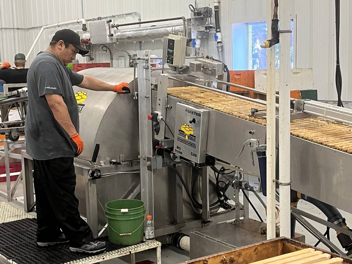 A worker at a honey processing facility overlooks a machine that extracts raw honey from the 