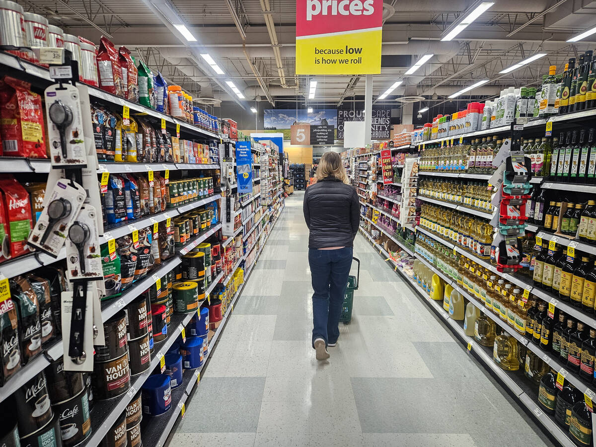 A woman walks away from the camera pushing a grocery cart up an aisle in a grocery store.
