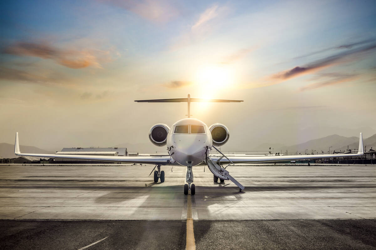 A stock image looking straight at the nose of a private jet sitting on a runway with the sun setting behind it.