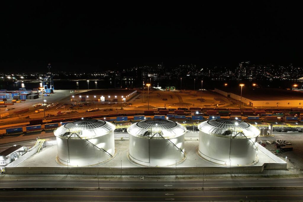 An aerial image of the DP World canola oil transloading facility taken at night, with three large storage tanks all lit up in the foreground.