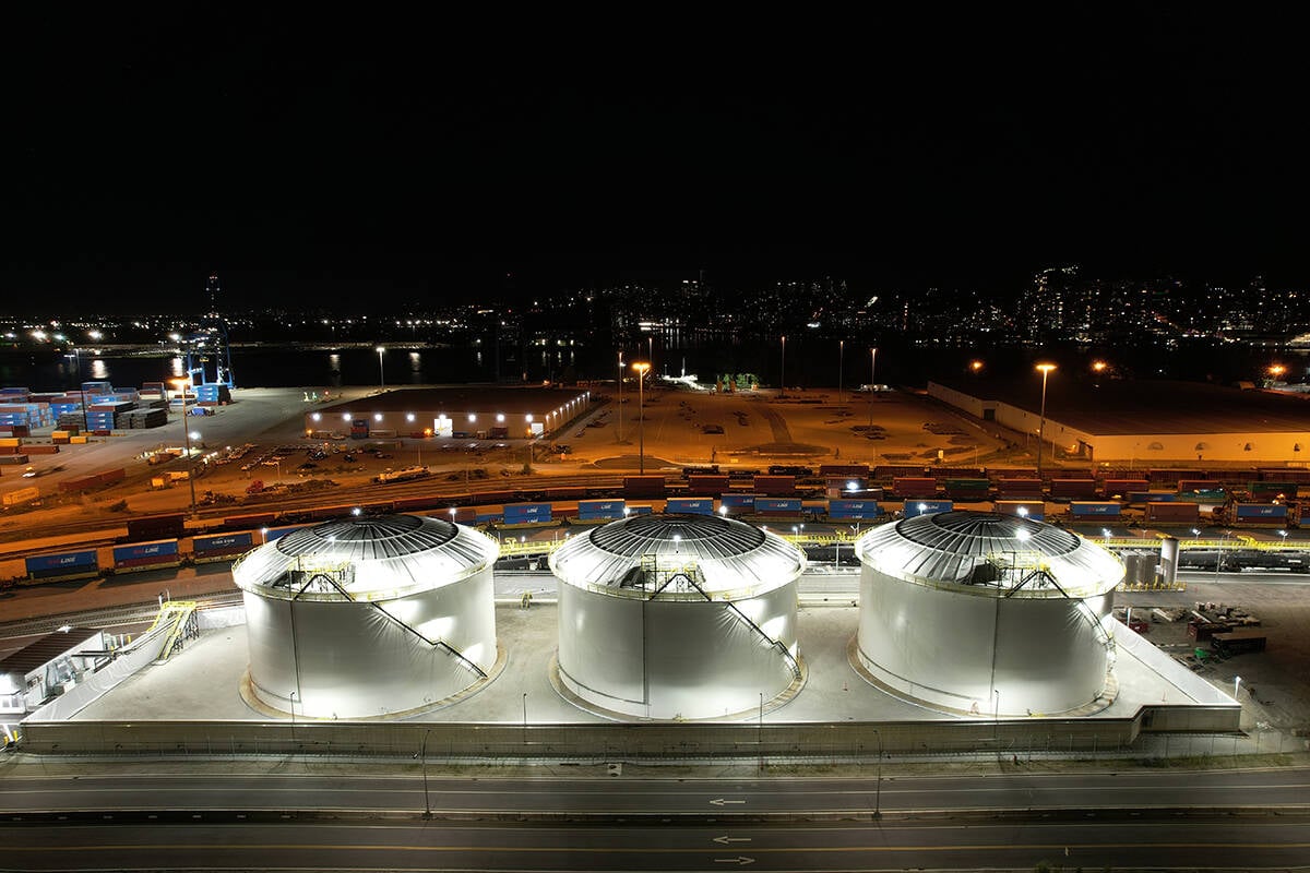 An aerial image of the DP World canola oil transloading facility taken at night, with three large storage tanks all lit up in the foreground.