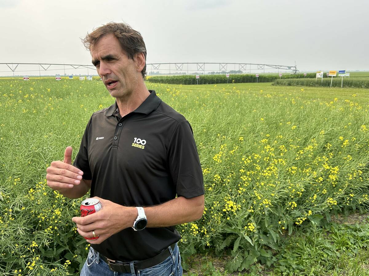 A man stands in front of a canola test plot with a section of pivot irrigation visible in the background.