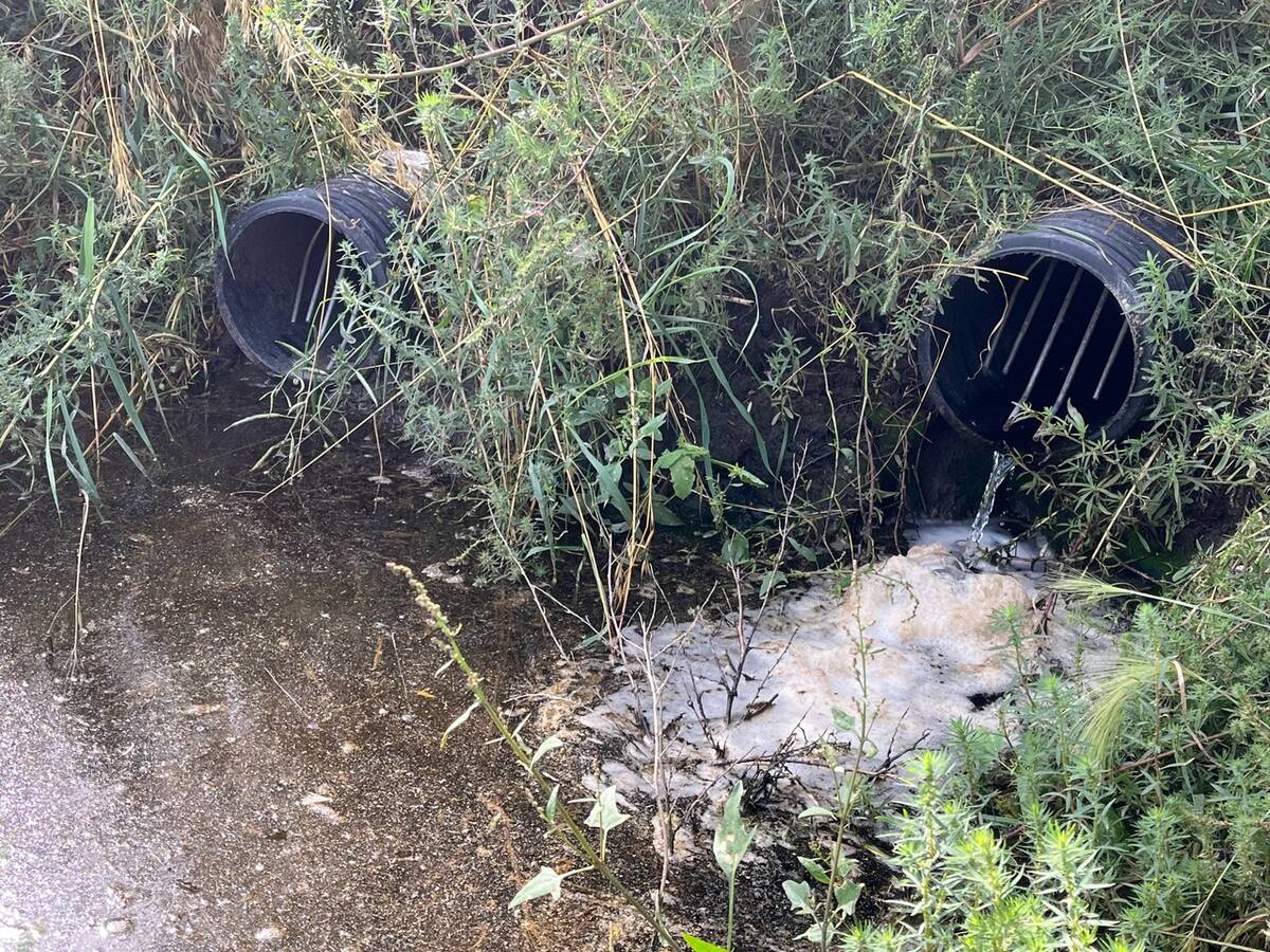 Two black plastic corrugated drainage pipes are seen draining water into a drainage ditch.