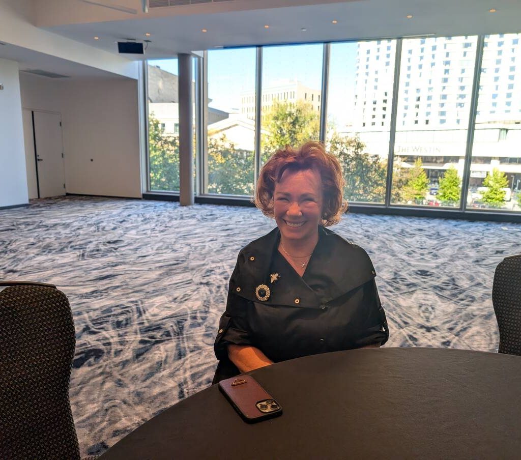 Arlene Dickinson smiles while sitting at a table in a meeting room.