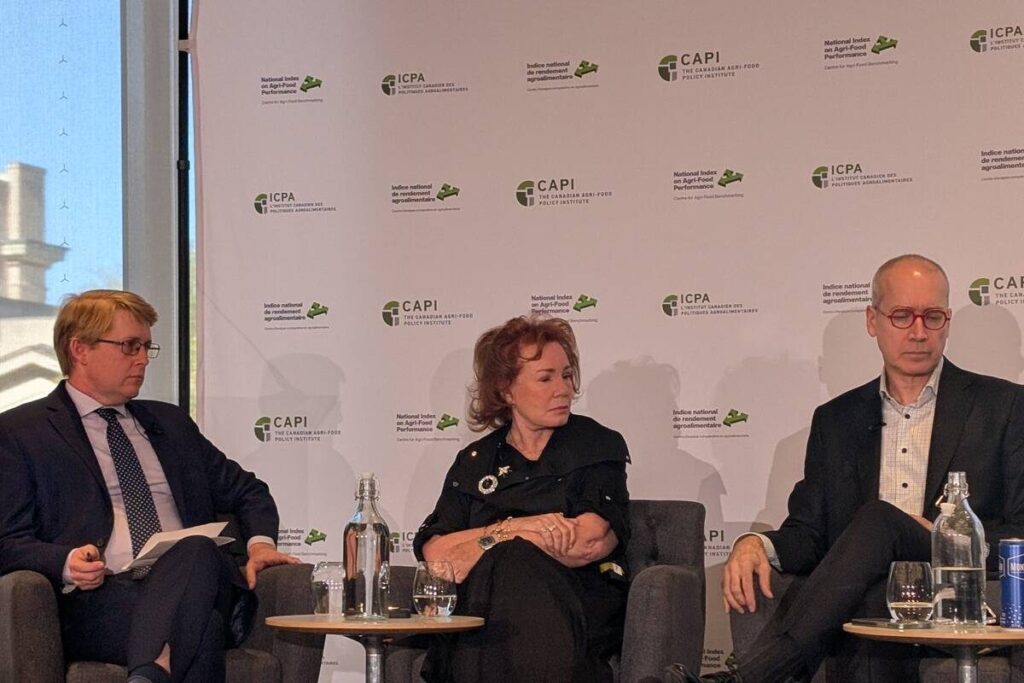 Arlene Dickinson sits between two men on a stage while speaking in a panel discussion.