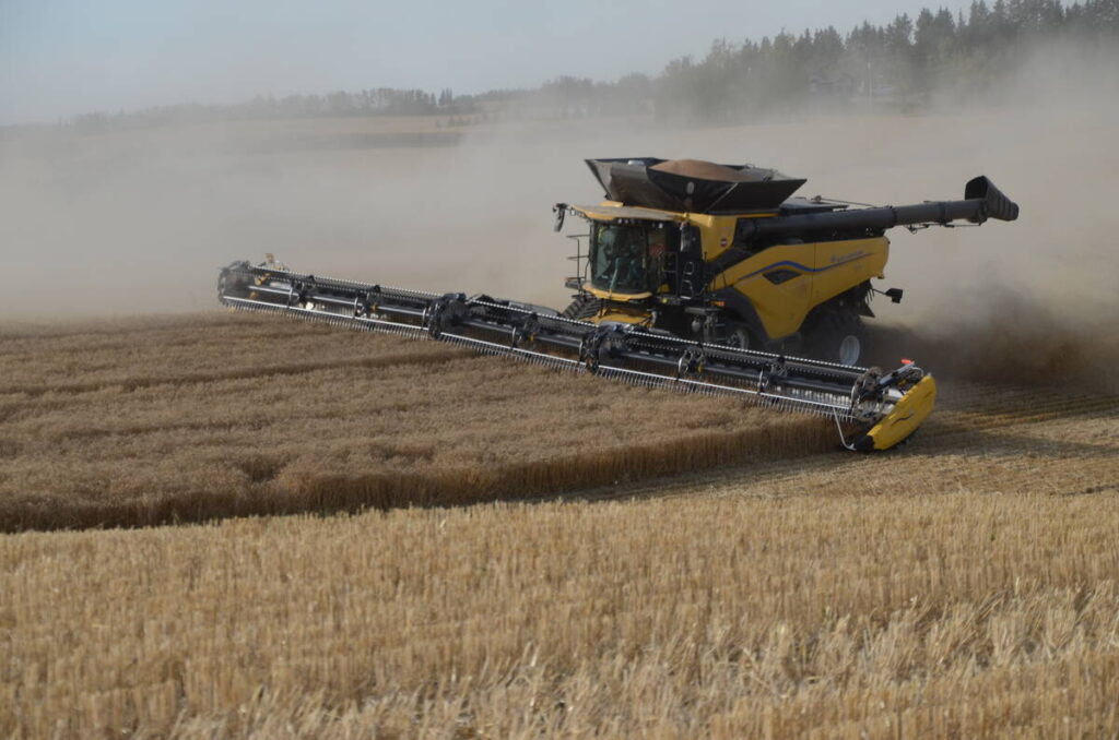 A yellow combine kicks up plenty of dust as it harvests a crop.