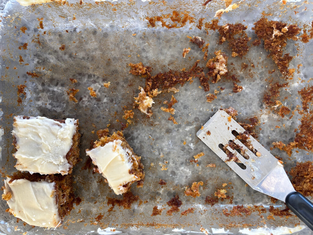 Three pieces of carrot cake and a spatula are all that remain in a large cake pan.