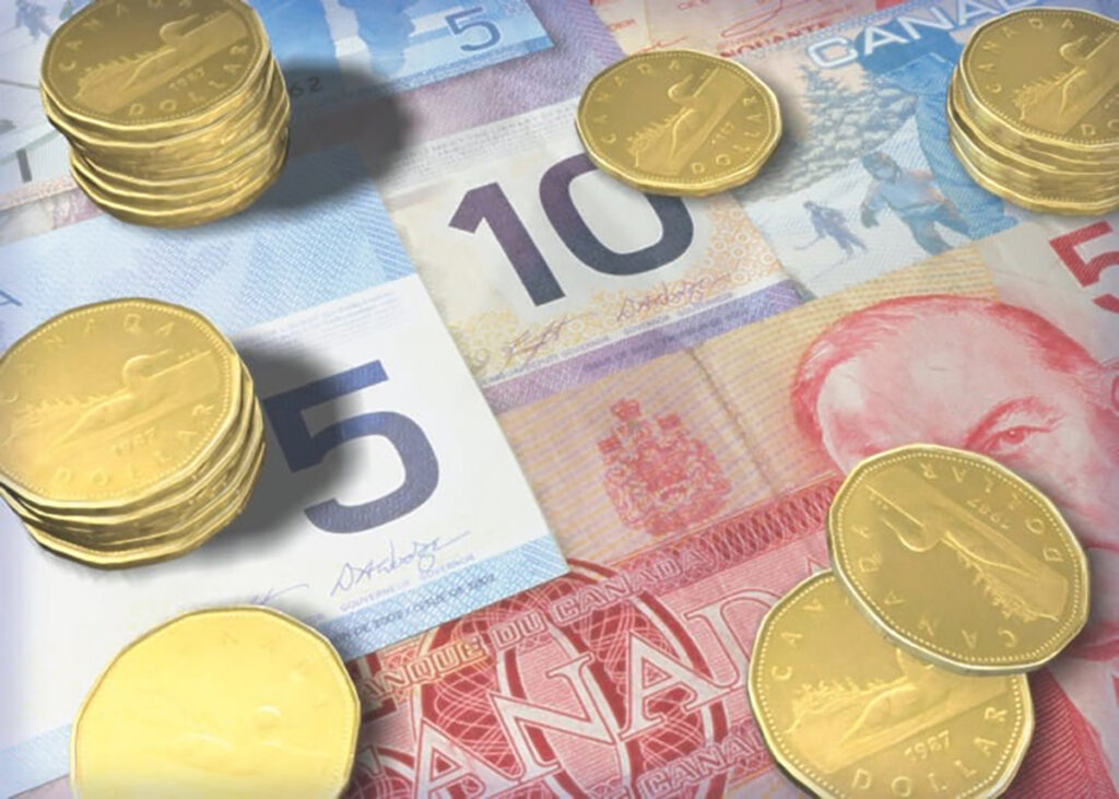 A variety of Canadian currency bills, ranging from $5 to $50, lay flat on a table with several short stacks of loonies on top of them.