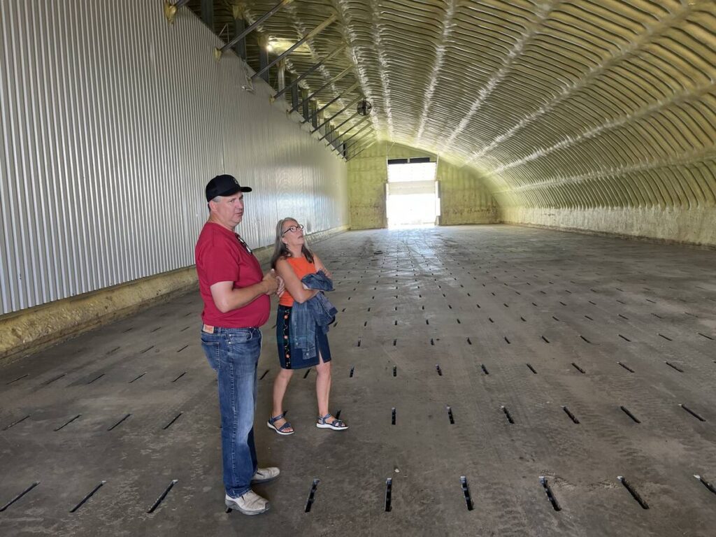 A man in a ball cap and a woman stand in a potato storage bin that has yellow spray foam insulation on its walls and curved ceiling.
