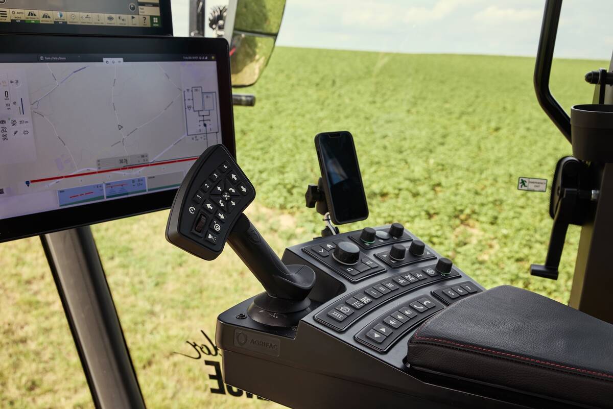 A view from inside the cab of a new Agrifac sprayer showing a laptop-sized screen, a control stick with multiple buttons on it and various other buttons on the dash.