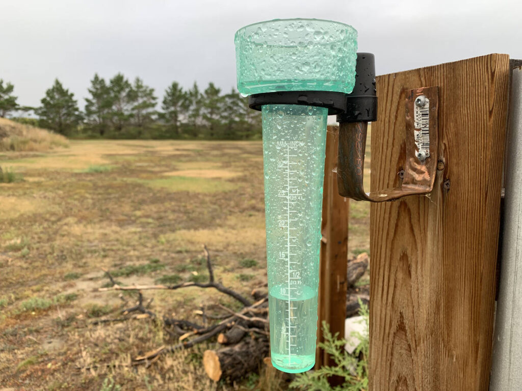 A rain gauge attached to a fence on a rural Prairie property shows about 10 ml of the precious liquid inside it.