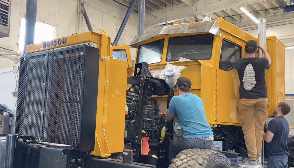Three men working on a large yellow truck with an