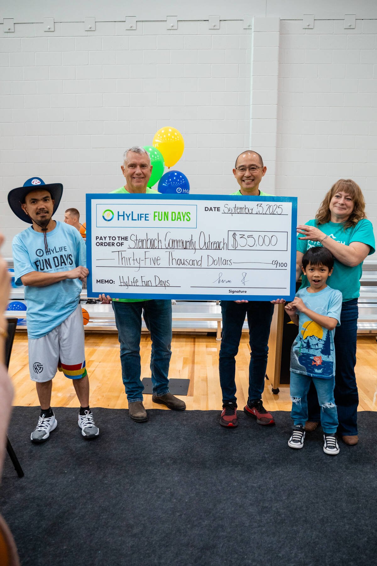 Four adults and a child stand in a gym holding a large cheque for $35,000 from HyLife Fun Days payable to