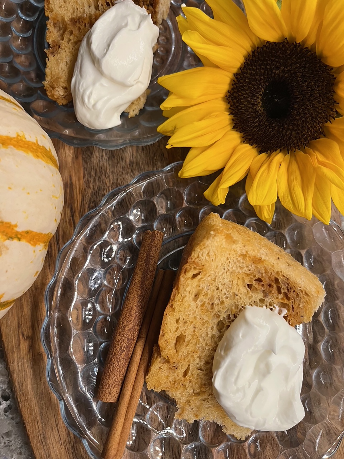 A slice of pumpkin angel food cake on a clear glass plate with a dollop of whipped cream on top and two cinnamon sticks beside it.