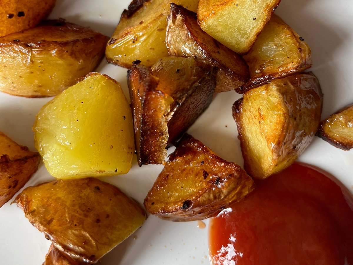 Cubed potatoes pan fried in duck fat on a white plate with a little ketchup.