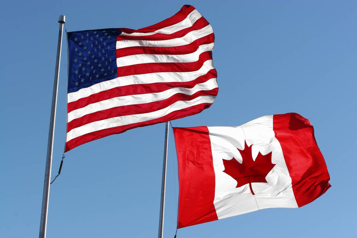 American and Canadian flags fly side-by-side against a clear blue sky background.