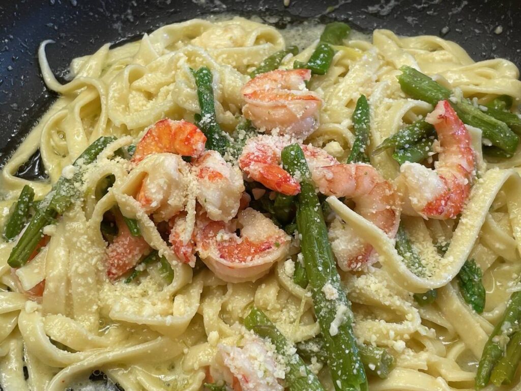 A close-up, overhead shot of shrimp fettuccini alfredo on a black dinner plate.