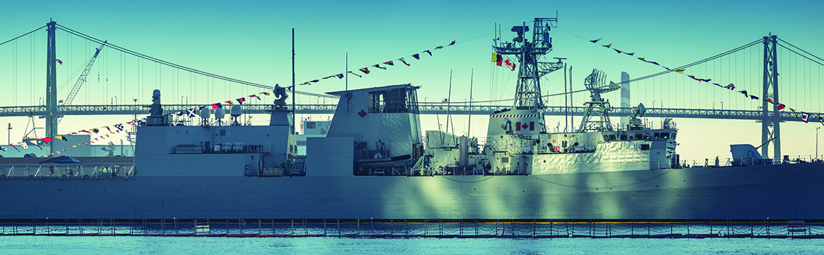 A Canadian Military warship is bathed in sunlight reflected off Purdy's Wharf Towers with the Angus L. MacDonald Bridge in the background.