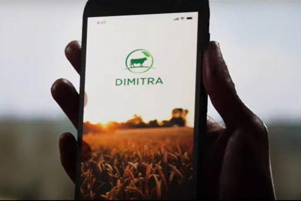 A farmers hand holds a mobile phone displaying the Dimitra Connected Farmer App