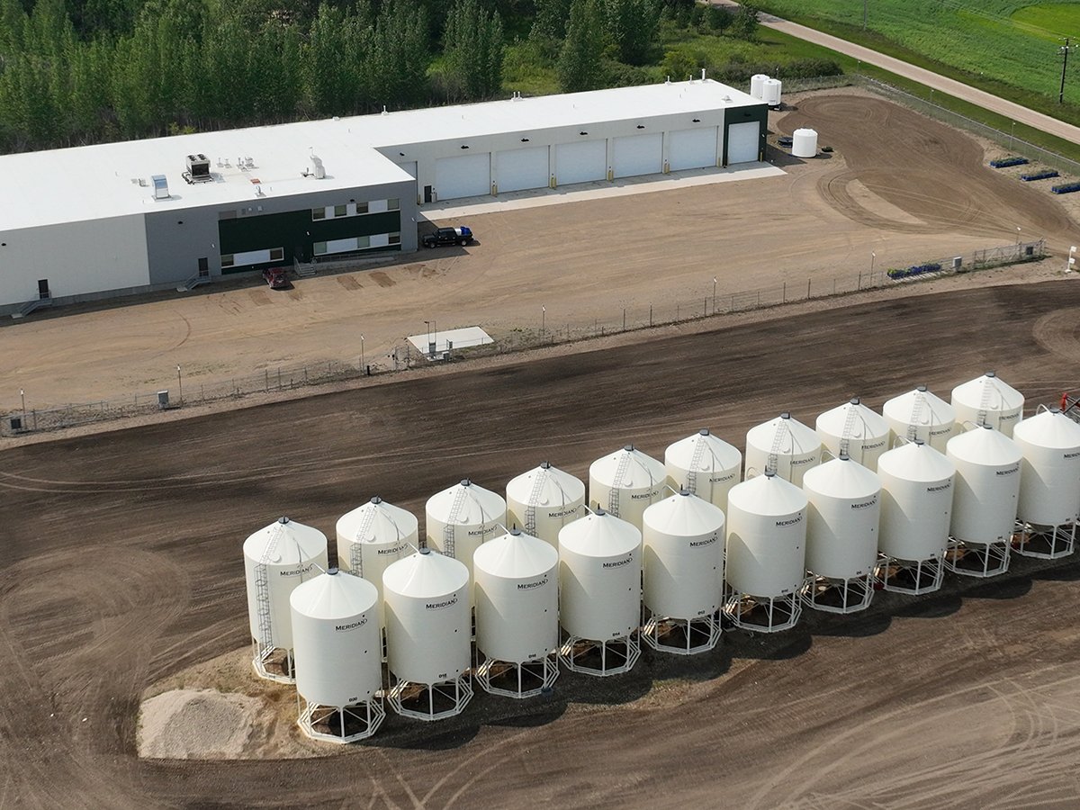 An aerial view of the Humaterra plant near Birch Hills, Saskatchewan, showing a large rectangular shop and 20 white upright smooth-walled hopper bins neatly positioned in two rows of 10.