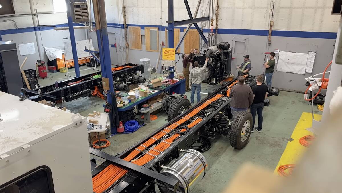 An overhead photo of an assembly team preparing to install a diesel generator onto a hybrid electric cab-over truck in a large shop.