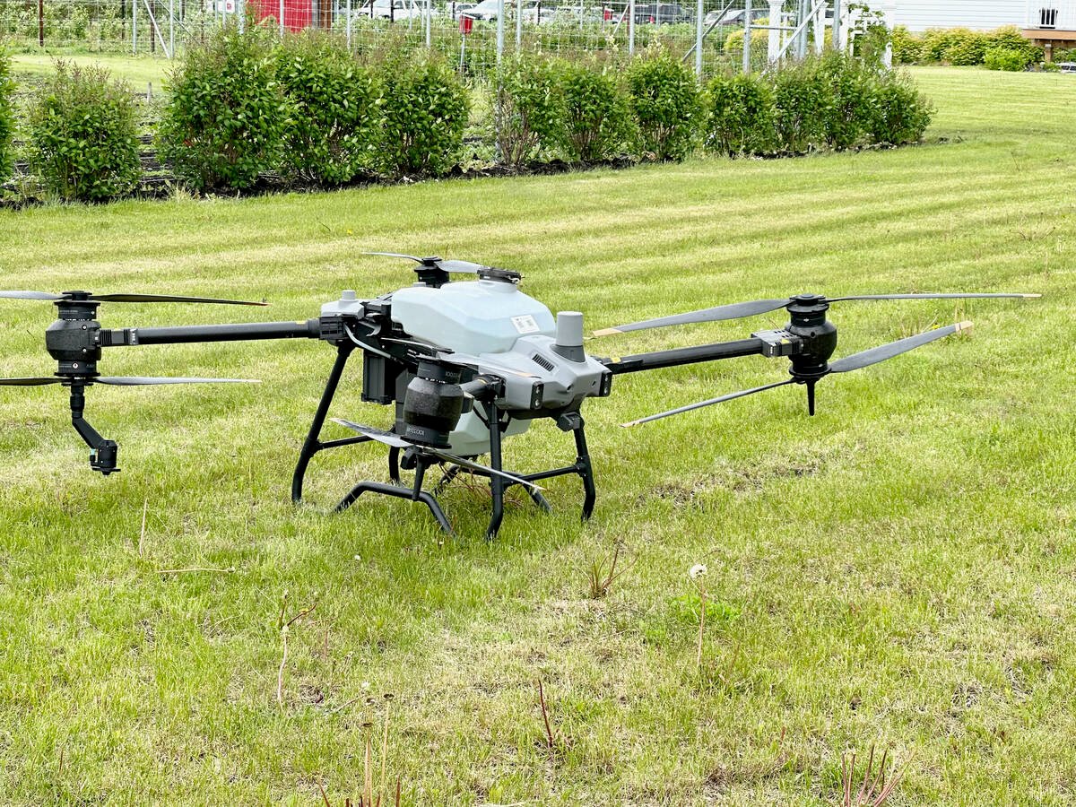 A large quad-copter style spray drone sits on the grass.