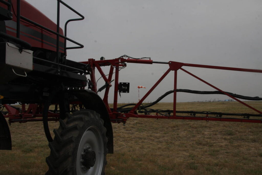 Close-up of the boom of a parked sprayer with a wind sock in the background on a cloudy day.