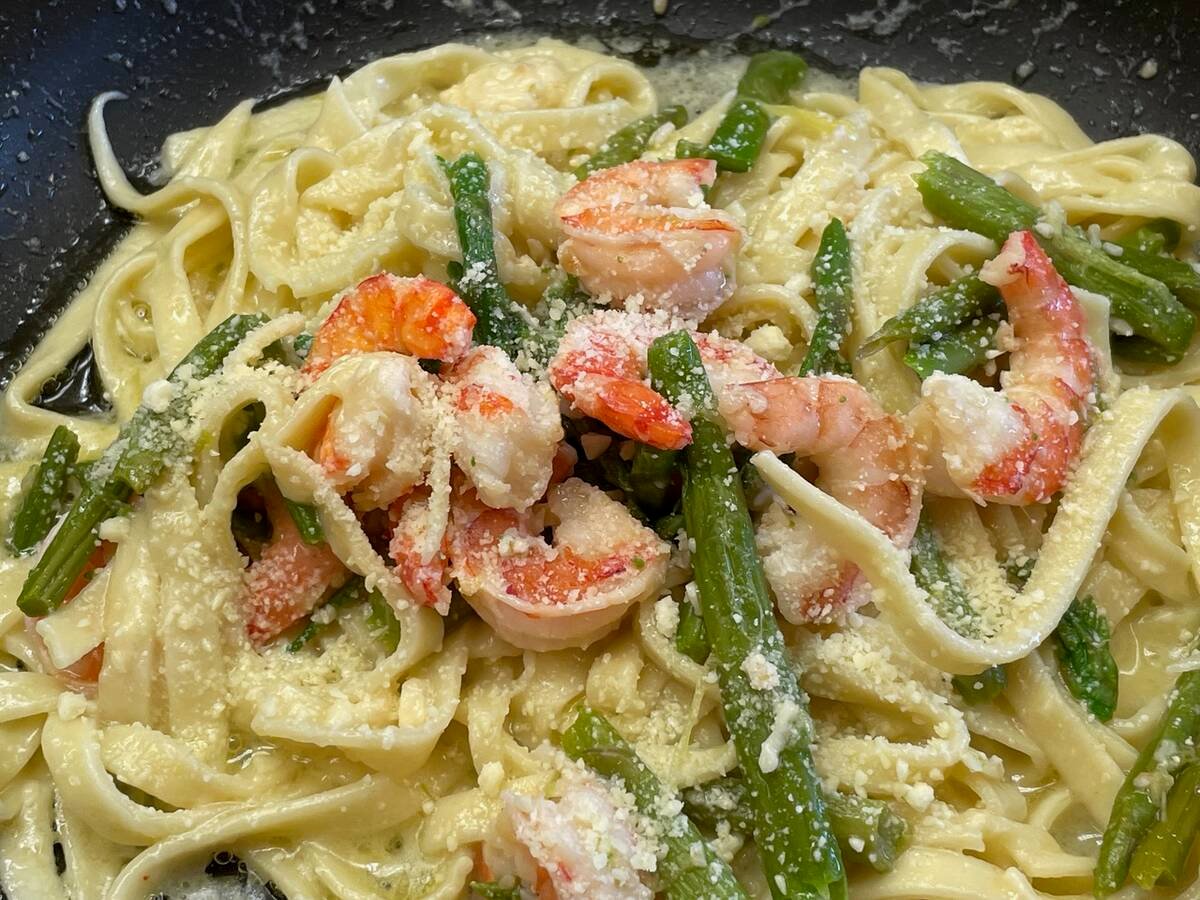 A close-up, overhead shot of shrimp fettuccini alfredo on a black dinner plate.