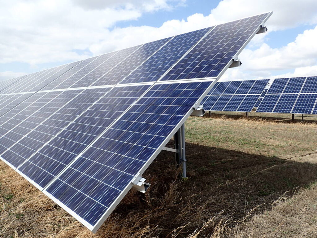 Two large arrays of solar panels are tilted upward toward the sun on a day with mixed sun and cloud.