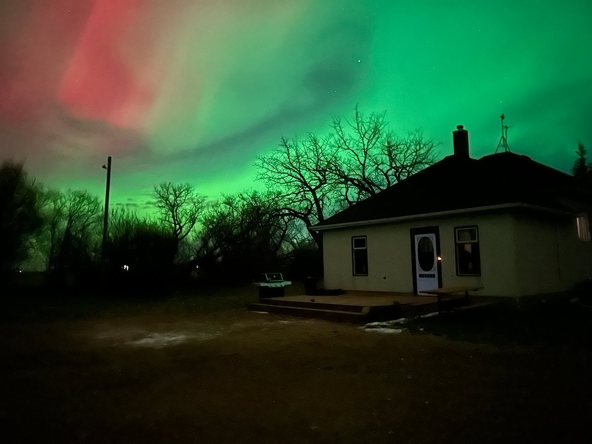 Red and green aurora light up the sky over a small farm house.
