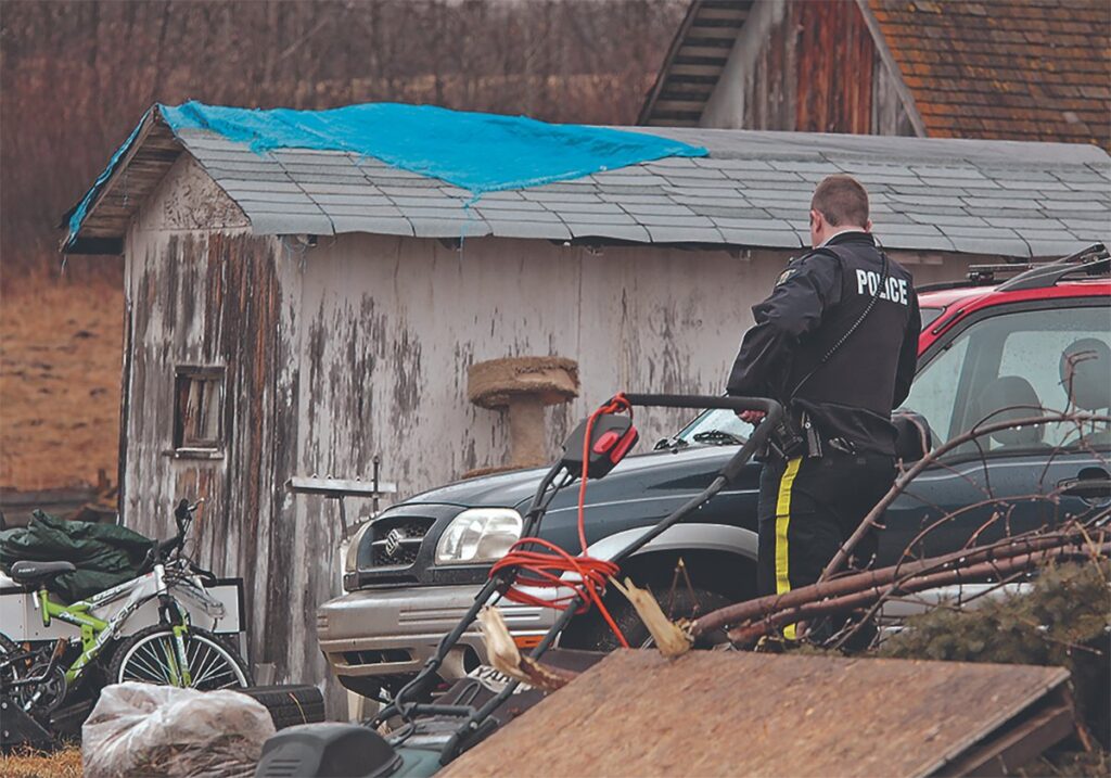 An RCMP officer looks around a cluttered rural yard.