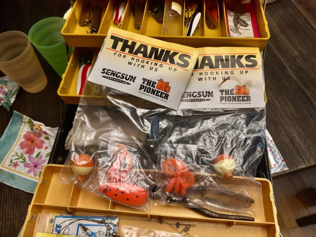 A yellow fishing tackle box sits open on a table with a number of lures in plastic bags on top with a label that reads, 