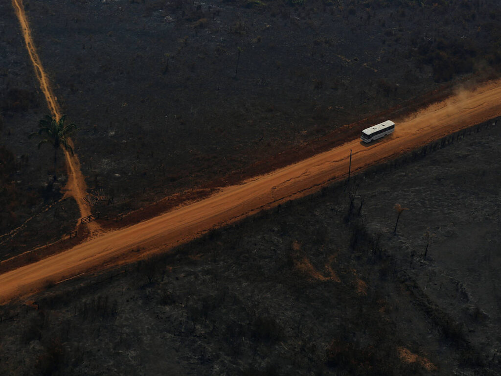 A an overhead drone photo of a bus driving along the Transamazon Highway as it passes through deforested and burnt land.