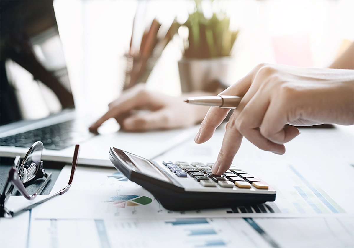 A close-up of hands on a calculator and laptop simultaneously.