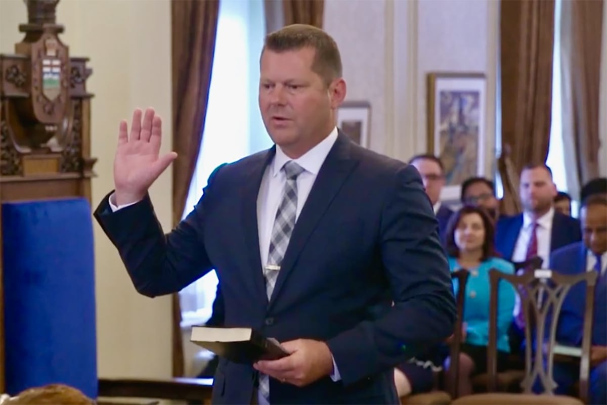 A man in a suit with his right hand raised and what appears to be a bible in his left takes some form of oath.