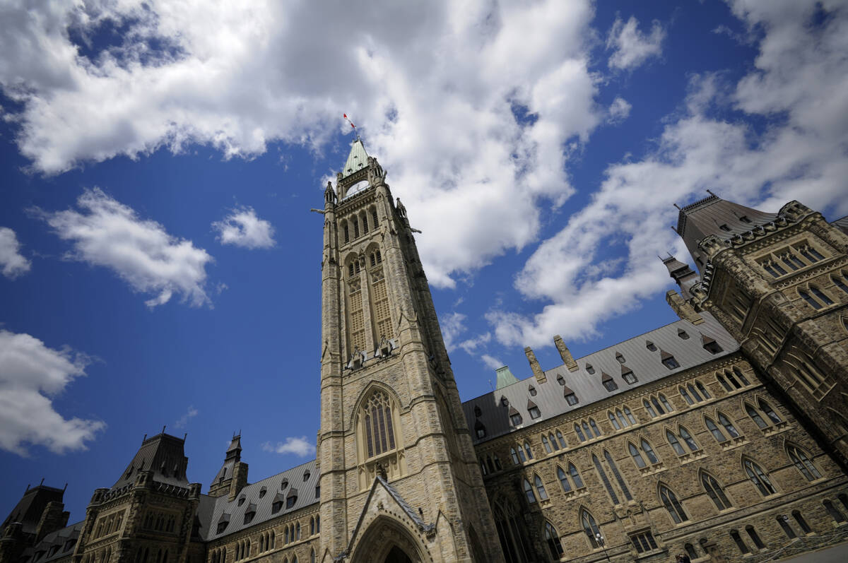 A view of the Peace Tower on Parliament Hill looking upward with a blue sky and a few clouds in the background.