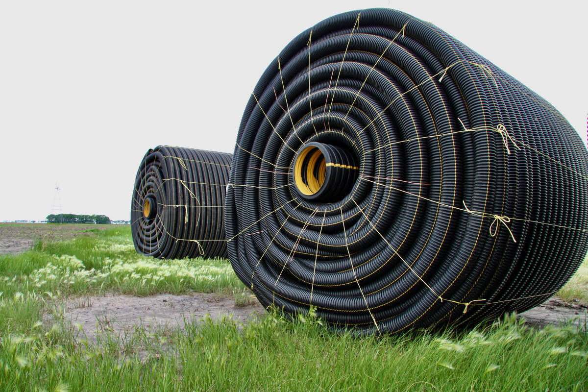 Two large rolls of tile drainage, perforated plastic pipe, sit, bound with twine, in a field waiting to be installed.