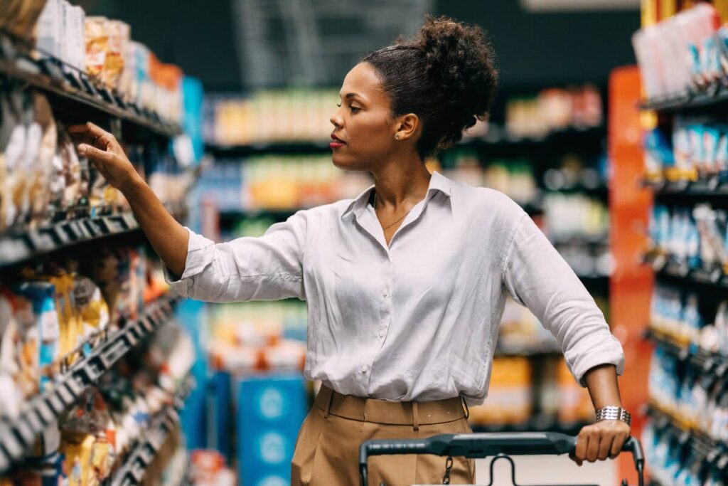 A thoughtful woman shops in a supermarket, browsing through products on the shelves.
