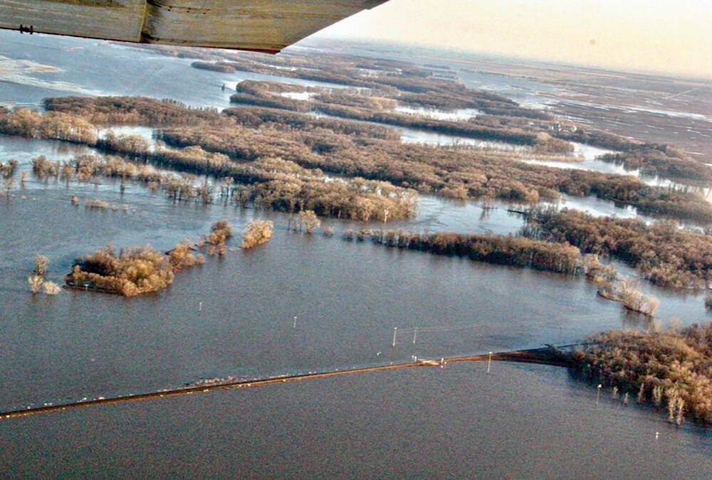 An aerial view of flooding in Manitoba in 2022 that shows a rural grid road just barely above the surface of water on both sides of it.