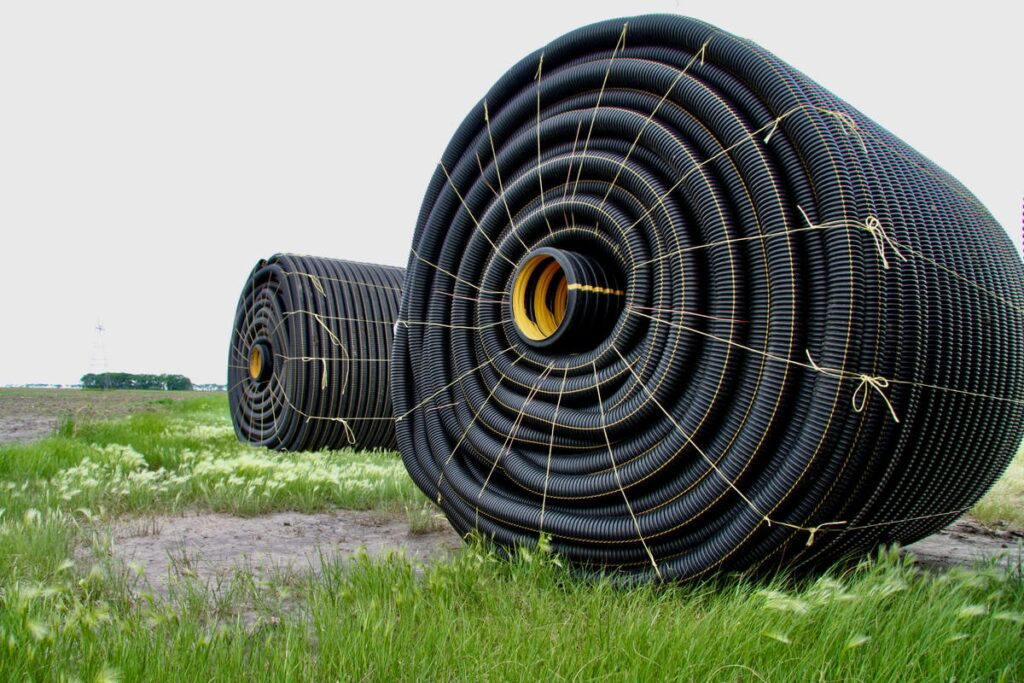 Two large rolls of tile drainage, perforated plastic pipe, sit, bound with twine, in a field waiting to be installed.