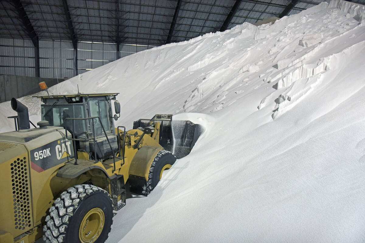 A wheel loader pushes its bucket into a massive pile of white fertilizer.