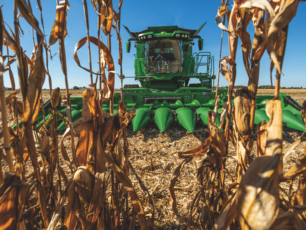 The corn header on a new John Deere combine is seen through a few cornstalks as the combine approaches.