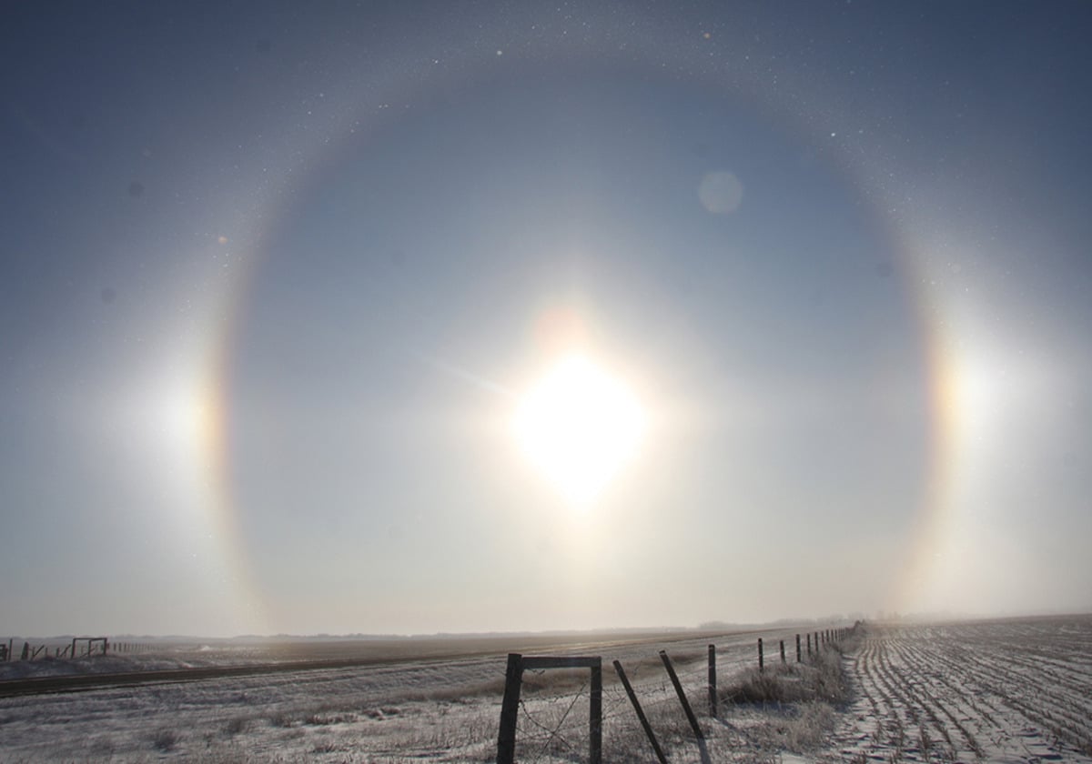 Sundogs form a perfect ring around the sun over a barbed wire fence line on a cold winter day.