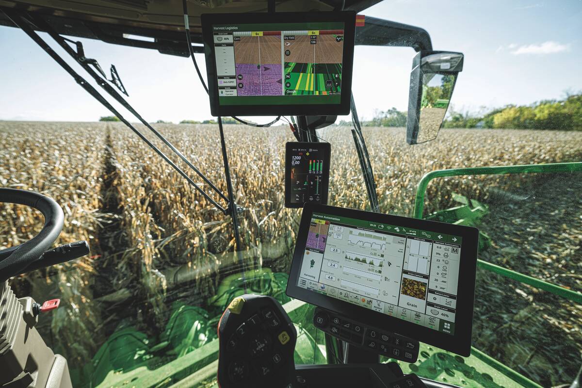 Inside the cab of a new John Deere combine as it harvests a corn crop showing three (two large, one smaller) computer screens for sharing combine data with the operator.