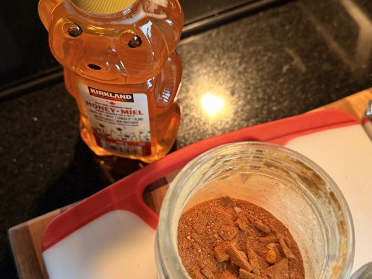 Looking down from above at a container of honey shaped like a bear and a round plastic container of reddish powder.