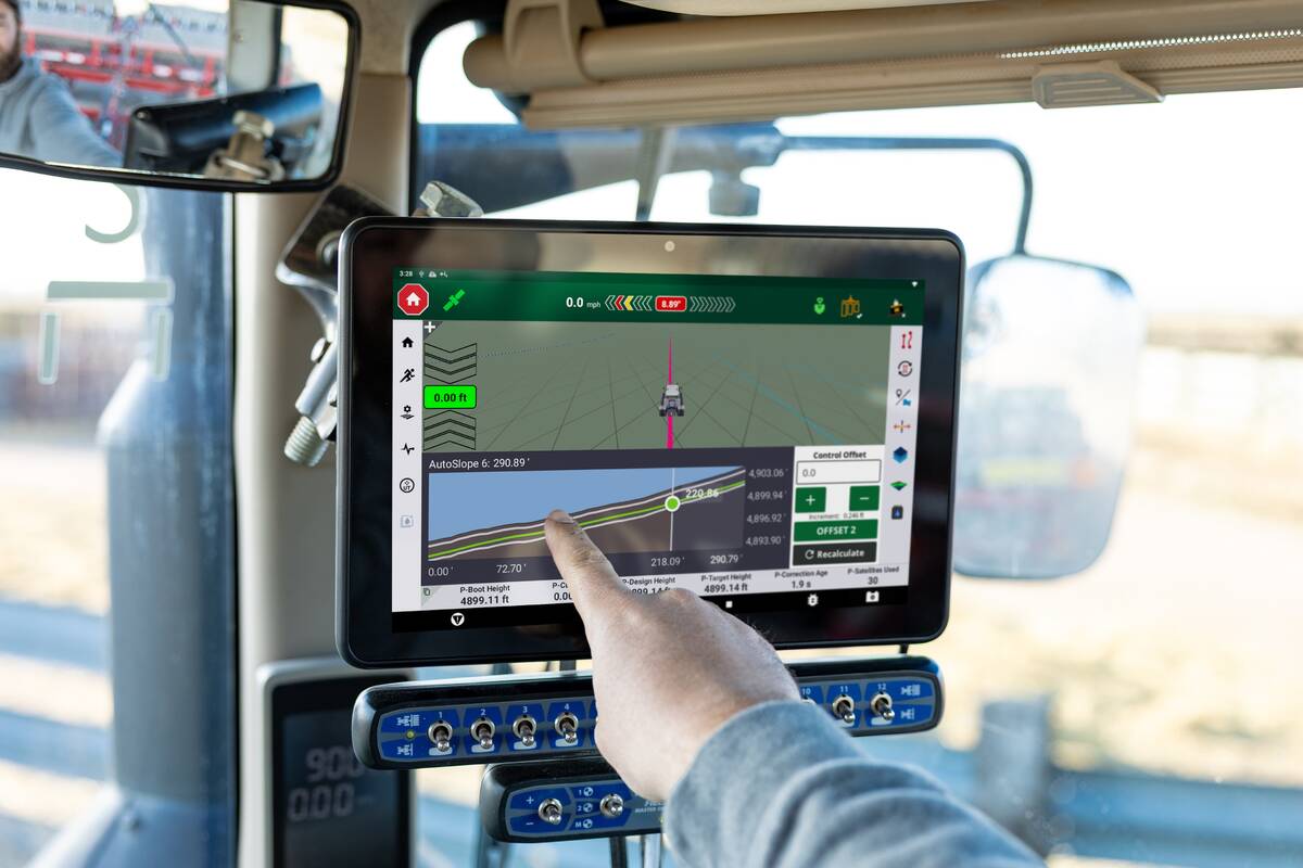 A man's index finger points at the display inside a tractor as the he operates it in the field.