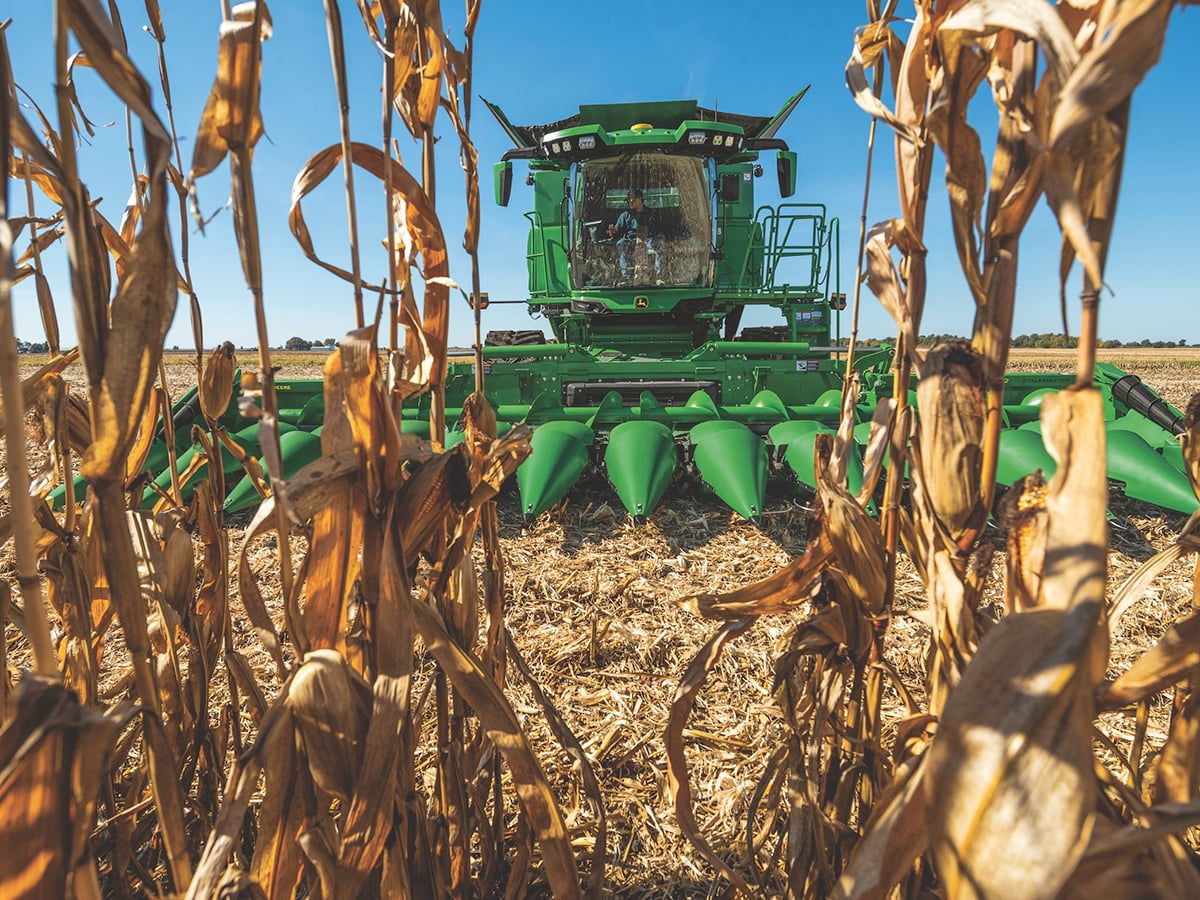 The corn header on a new John Deere combine is seen through a few cornstalks as the combine approaches.