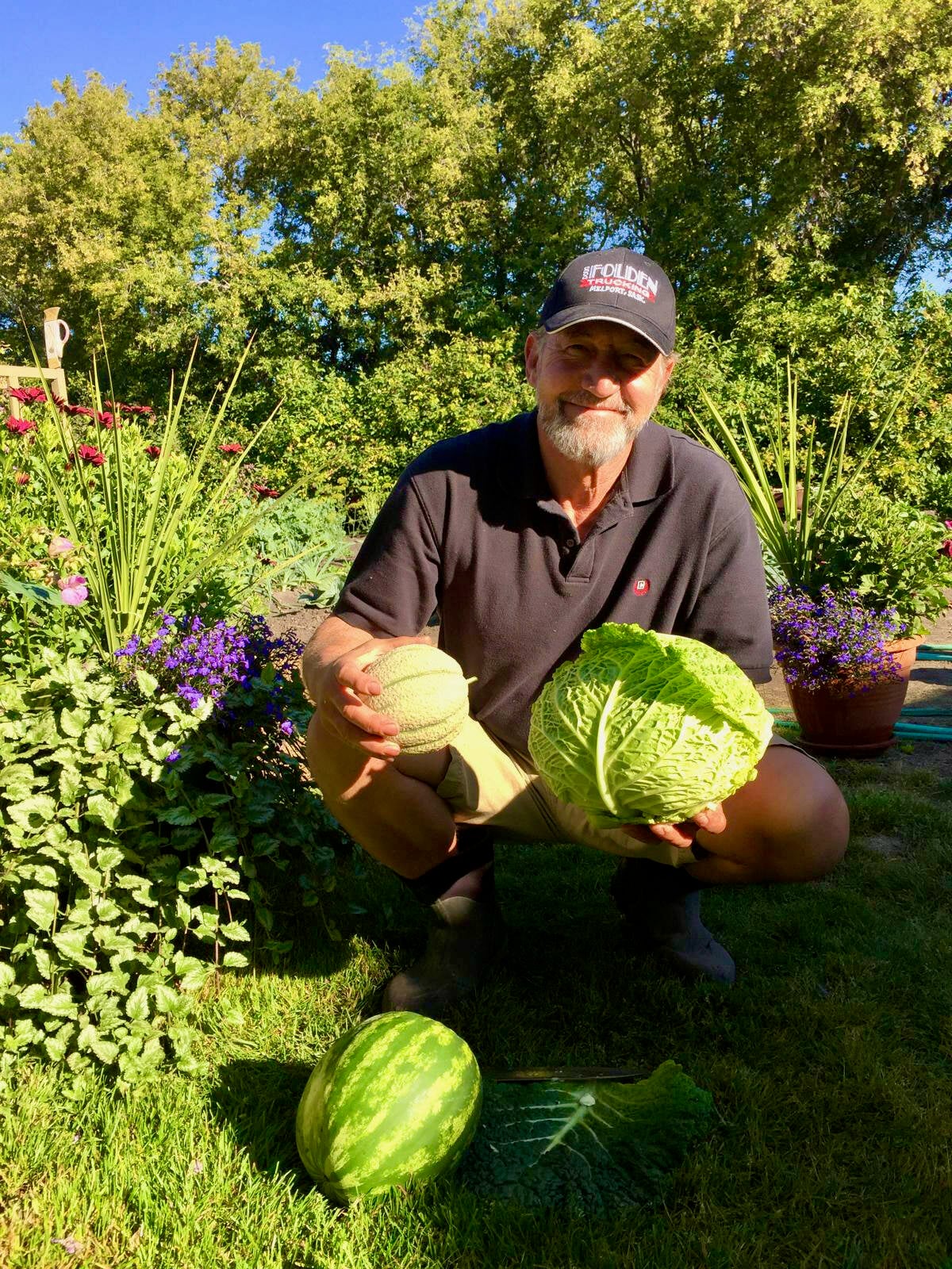 Peter Schemenauer crouches in his garden while holding a head of lettuce in one hand and a squash in the other on a sunny summer day near Englefeld, Sask.