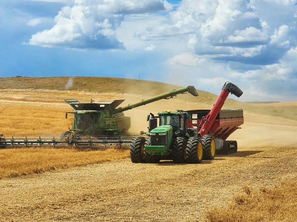 A combine and a tractor pulling a grain cart are side by side in this screencap from the Monette Farms website.