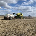 An air seeder rig seeds red lentils on a sunny day, with a number of pillowy white clouds in the sky, southeast of Delisle, Saskatchewan.